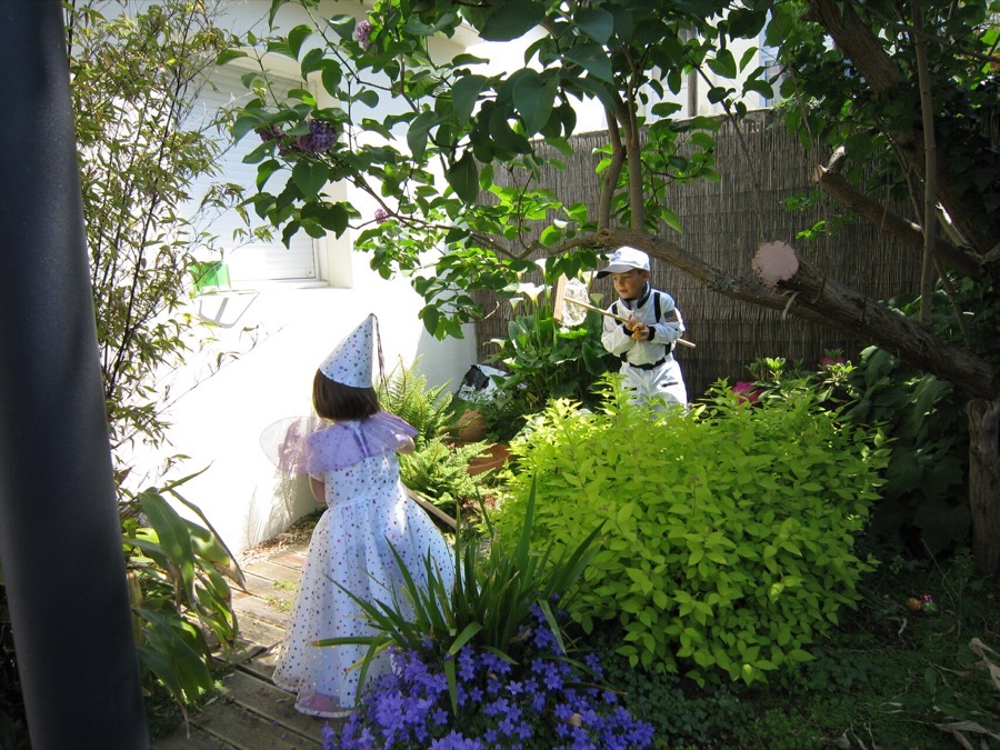 Two children in costume — a fairy and an astronaut — exploring a sunlit garden